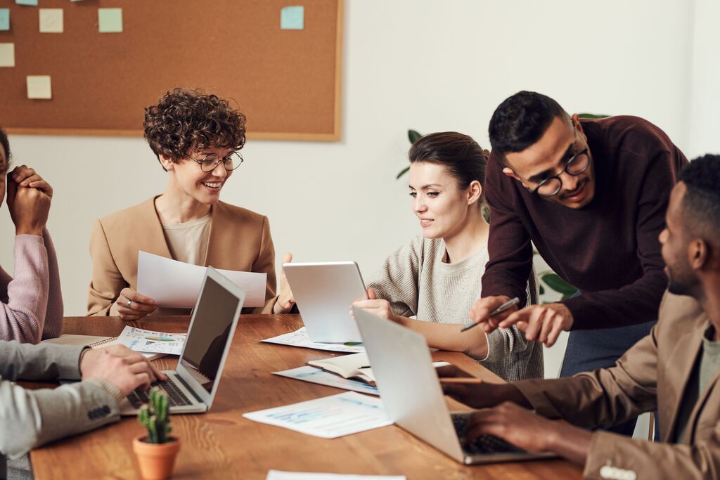 Personas diversas alrededor de una mesa de oficina con notebooks y documentos trabajando en equipo.